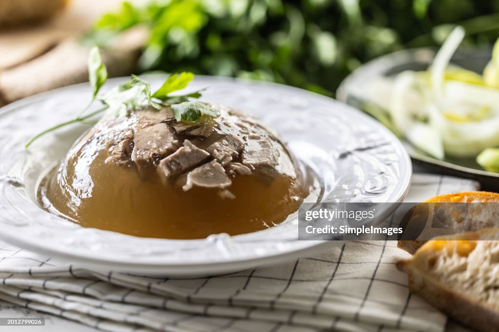 Homemade pork aspic, meat jelly with onion and leek in a white plate