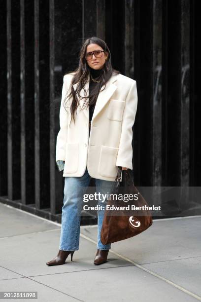 Guest wears sunglasses, a white oversized blazer jacket , a brown suede Gucci bag, blue denim jeans pants, high heels pointed leather bag , during...