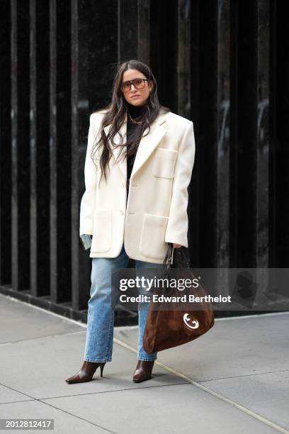 Guest wears sunglasses, a white oversized blazer jacket , a brown suede Gucci bag, blue denim jeans pants, high heels pointed leather bag , during...