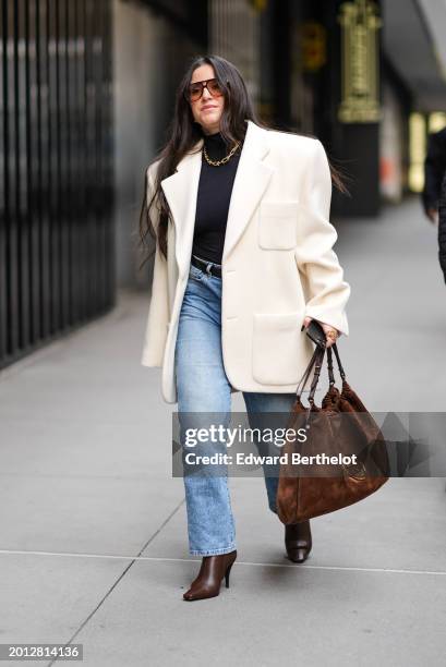 Guest wears sunglasses, a white oversized blazer jacket , a brown suede Gucci bag, blue denim jeans pants, high heels pointed leather bag , during...