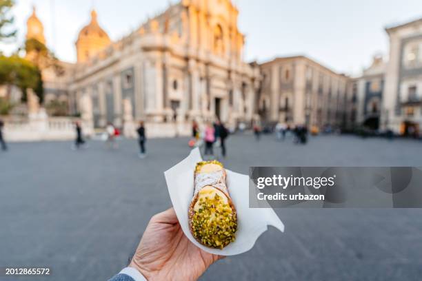 young man holding a cannoli pastry filled with creamy ricotta and pistachios on the street in catania, sicily - val di noto stock pictures, royalty-free photos & images