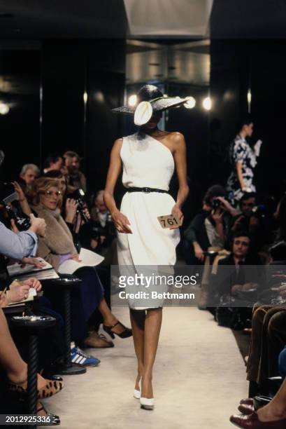 Model wearing a white one-shoulder dress and a black hat adorned with a white lily from Chanel's collection for spring and summer, Paris, January...