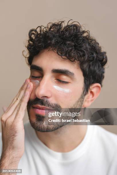 portrait of a young man applying moisturiser on his face. - massaggio del viso foto e immagini stock