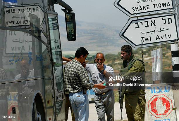 An Israeli soldier questions a Palestinian passenger as the driver of an Arab bus stands nearby May 19, 2003 at the Tapuah junction military...