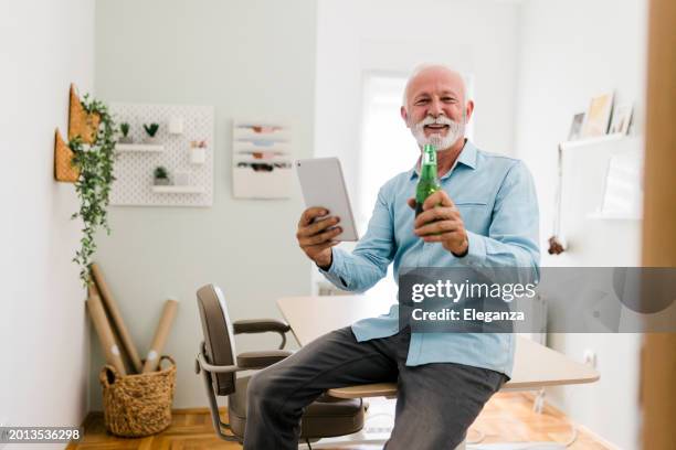 senior man drinking beer while having video call on his digital tablet - online happy hour stock pictures, royalty-free photos & images