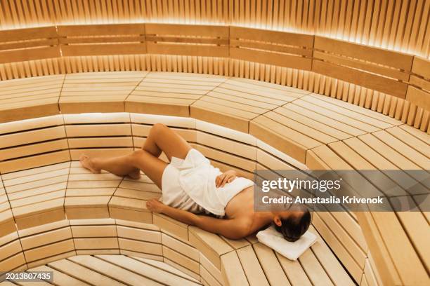 young woman relaxing and sweating in hot sauna wrapped in towel. - cipresso stock-fotos und bilder