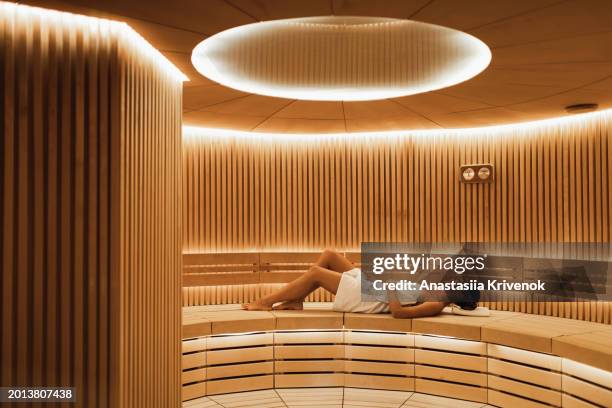 young woman relaxing and sweating in hot sauna wrapped in towel. - cipresso stock-fotos und bilder