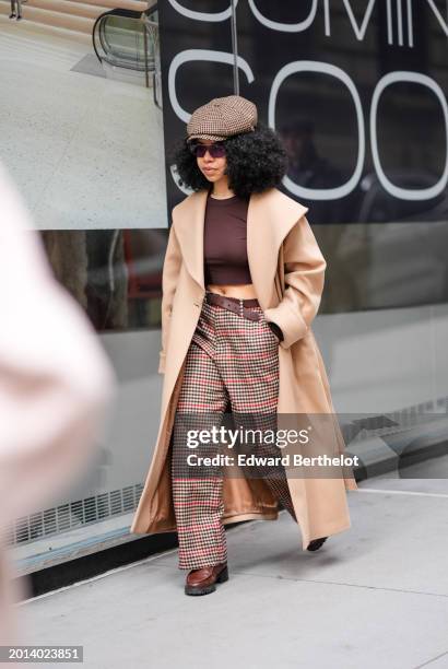 Guest wears a paperboy hat in beige houndstooth printed pattern, sunglasses, a beige long coat, a brown crop top, a belt, flared pants in checkered /...
