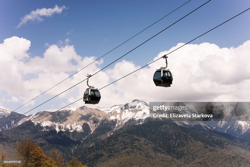 Cable car and lifts on the background of snowy mountains outdoors. The background of the landscape. Picturesque view of snowy mountains among clouds of clouds and clear sky. A place for the text. Sochi. Krasnaya Polyana. Copy space