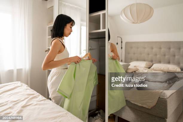 asian woman taking her work clothes out of her closet - medical scrubs hanger stock pictures, royalty-free photos & images