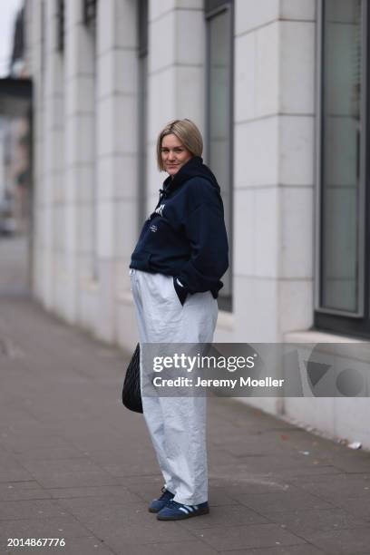 Victoria Thomas seen wearing gold earrings, Hernameis navy blue oversized cotton logo pattern hooded sweater, Hernameis white / blue striped long...