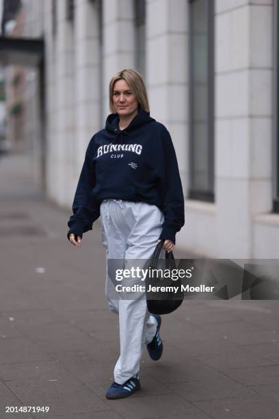 Victoria Thomas seen wearing gold earrings, Hernameis navy blue oversized cotton logo pattern hooded sweater, Hernameis white / blue striped long...