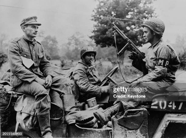 Pfc Louis Barrett of the United States Army's Military Police, United States First Army sits behind the wheel of a Willys Jeep while Private RFD...