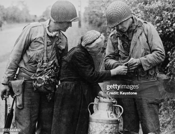 Private Carl Rendleman, United States First Army uses a French-English phrase book to explain to a local French woman that she cannot pass on the N13...