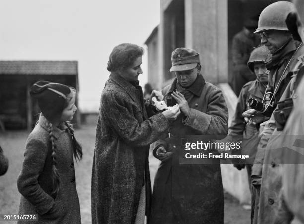 German civilian woman bandages the hand of a young teenage Wehrmacht conscript soldier after surrendering to a unit from the United States Ninth Army...