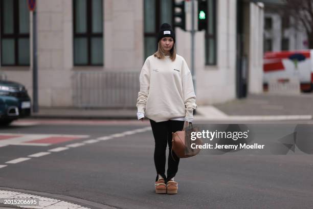 Elise Rozay seen wearing gold earrings, Hernameis black wool knit logo patch beanie, Hernameis creamy white logo print pattern oversized sweater,...