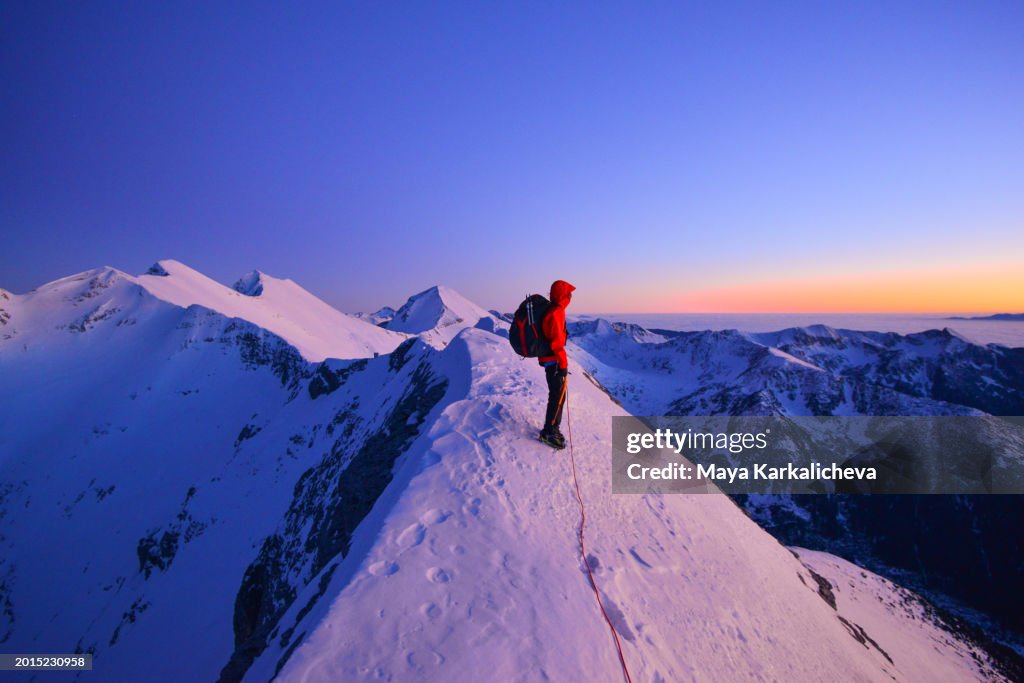 Mountaineer reaching the summit on snowcapped ridge at dusk