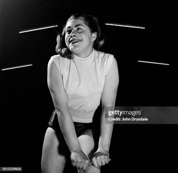 Seventeen-year-old Margaret Mawer bending a six-inch nail, wrapped to protect her hands, over her thigh, London, January 1956. Margaret, who is an...