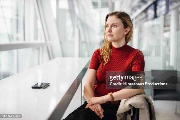 woman looks out window while waiting for flight in airport lounge - woman blond looking left window stockfoto's en -beelden