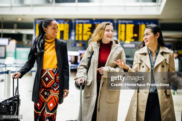 three businesswomen chat while on their way to catch a flight - long coat stock pictures, royalty-free photos & images