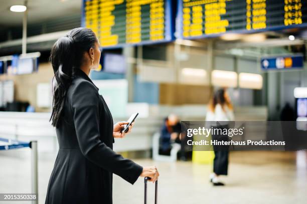 businesswoman checks the flight information board at an airport - business travel stock pictures, royalty-free photos & images