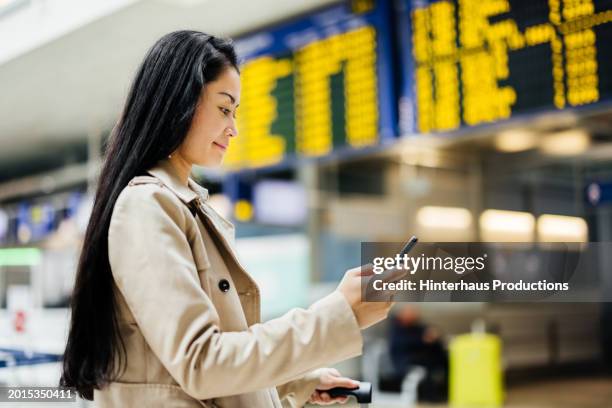 woman with long hair looks at smartphone in airport - cream coloured jacket stock pictures, royalty-free photos & images