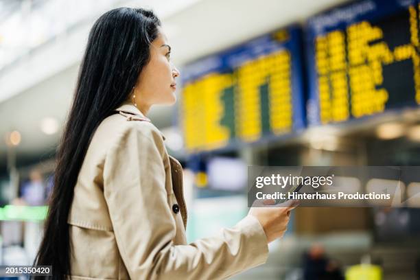a woman checks her flight details at an airport - cream coloured jacket stock pictures, royalty-free photos & images