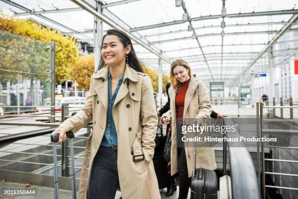 three women exit airport via an escalator - long coat stock pictures, royalty-free photos & images
