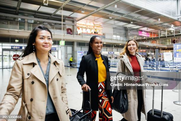 three friends make their way through an airport together - long coat stock pictures, royalty-free photos & images