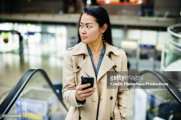 young woman climbing escalator in airport - long coat stock pictures, royalty-free photos & images