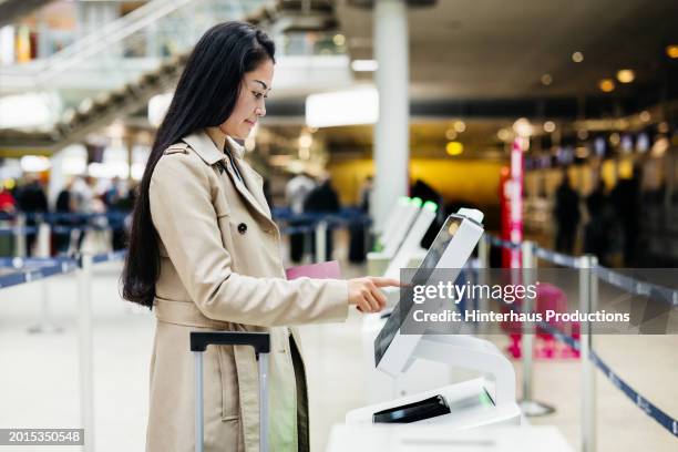 woman uses self-service check-in kiosk before catching flight - long coat stock pictures, royalty-free photos & images