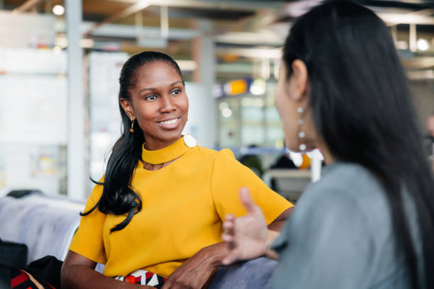 glamorous woman wearing yellow talks to friend while waiting for a flight - communication stock pictures, royalty-free photos & images