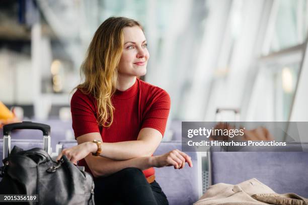 elegant woman smiles while waiting in an airport lounge - abflugbereich stock-fotos und bilder