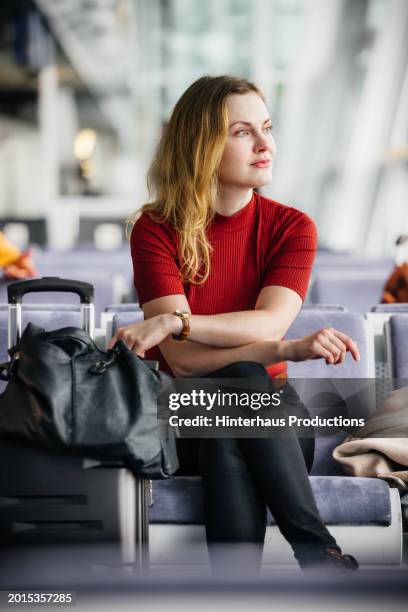 an elegant woman looks out a window waiting for her flight - woman blond looking left window stockfoto's en -beelden