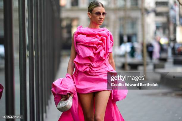 Guest wears sunglasses, a neon pink ruffled floral embroidery oversized long and mini dress / gown , outside Carolina Herrera, during New York...