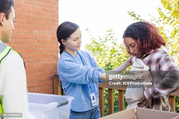 woman holds donated shirt up to female friend - man holding donation box stock pictures, royalty-free photos & images