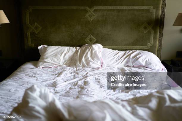 a bed with white sheets and large pillows, headboard with a dark green design, half of two lamps are visible - headboard stock pictures, royalty-free photos & images