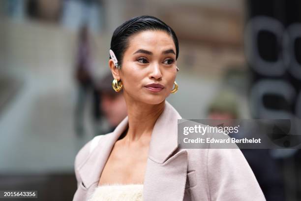 Guest wears hair pins, golden earrings, mauve lipstick, make-up , a coat, during New York Fashion Week, on February 12, 2024 in New York City.