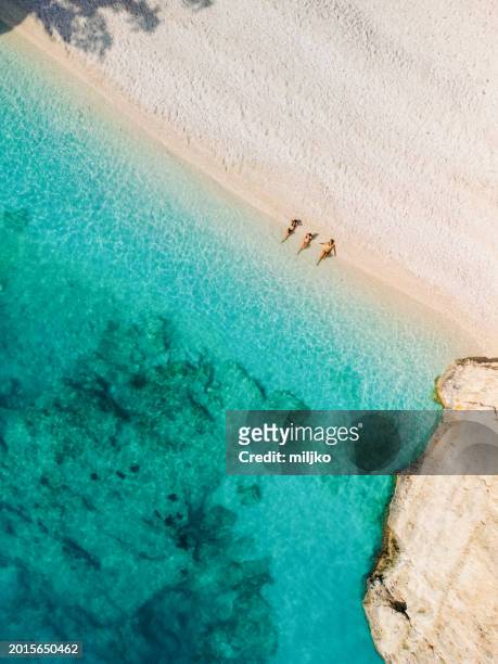 people relaxing and aunbathing on beach with clear sea water - cefalónia imagens e fotografias de stock