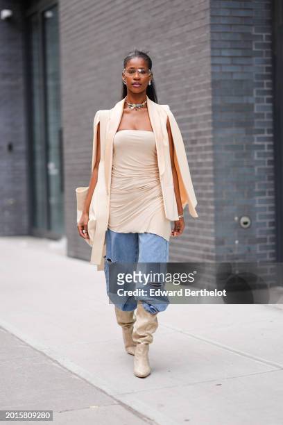 Guest wears glasses, a necklace, a beige oversized blazer jacket, a gathered low-neck off-shoulder top, blue ripped denim jeans pants , beige leather...