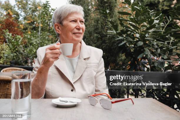 happy woman 60-69 years old drinks coffee in a cafe on the summer veranda - croatia stock pictures, royalty-free photos & images