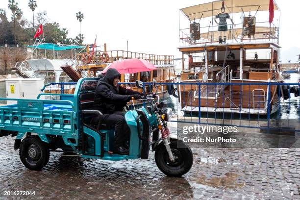 People drive a motorcycle in a rain near yachts in a harbour in Antalya, a tourist resort in southern region of the Republic of Turkiye on February...