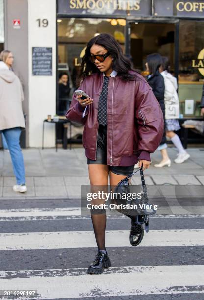 Guest wears burgundy dark red bomber jacket oversized, black Balenciaga bag, tie, shorts outside Bora Aksu during London Fashion Week February 2024...