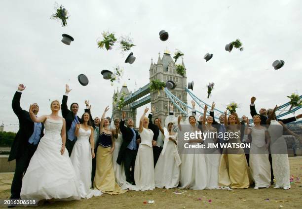 Twelve brides and grooms throw their hats and bouquets in the air in front of the Tower Bridge in London, 21 August 2003 to celebrate the London...