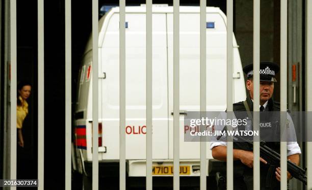 Heavily armed London police officer stands guard behind the barred gate of Belmarsh Magistrates Court as a woman closes the security garage door...