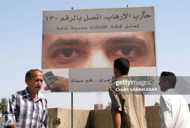 Iraqis walk past a bill board advertising a free phone number for people to call in and report militant activity 27 July 2005, in Baghdad. The bill...