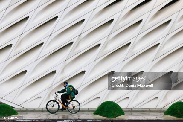 Los Angeles, CA A person rides a bike in front of The Broad museum during a Presidents Day rain storm downtown on Monday, Feb. 19, 2024 in Los...