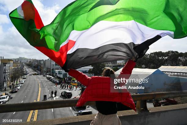 Woman holds a Palestinian flag while thousands of protesters, holding banners and Palestinian flags, gather outside of City Hall to march on Market...