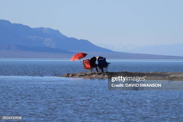 People relax by the water's edge as they enjoy the rare opportunity to see water during their visit to Badwater Basin, the normally driest place in...