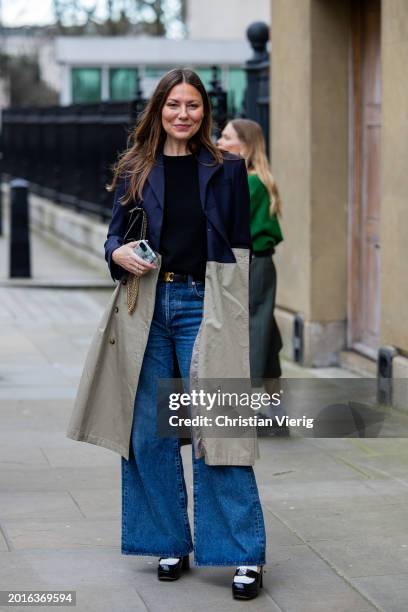 Guest wears beige navy two tone coat, flared wide leg denim jeans, Celine belt outside Huishan Zhang during London Fashion Week February 2024 on...
